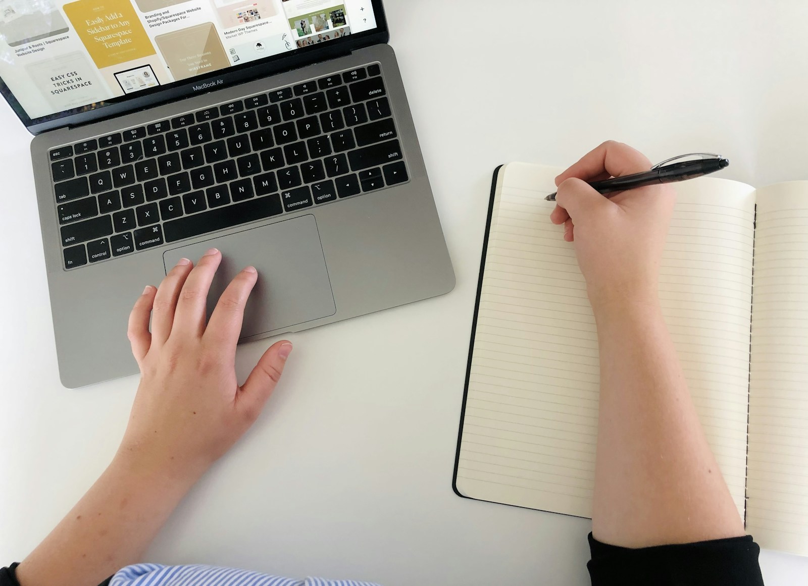 A person writing in a notebook while working on a laptop