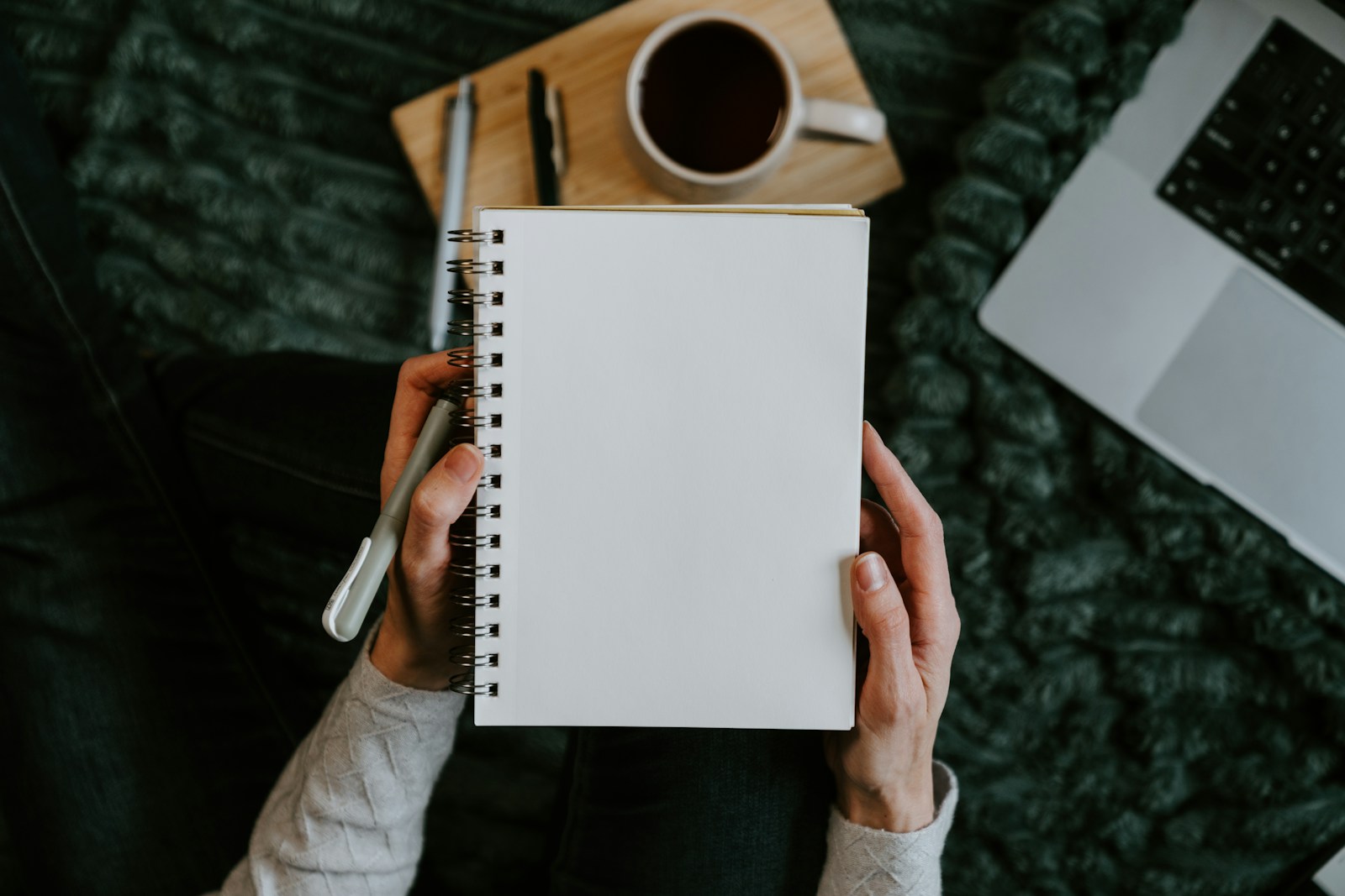 Hands holding a blank notebook beside a laptop and coffee